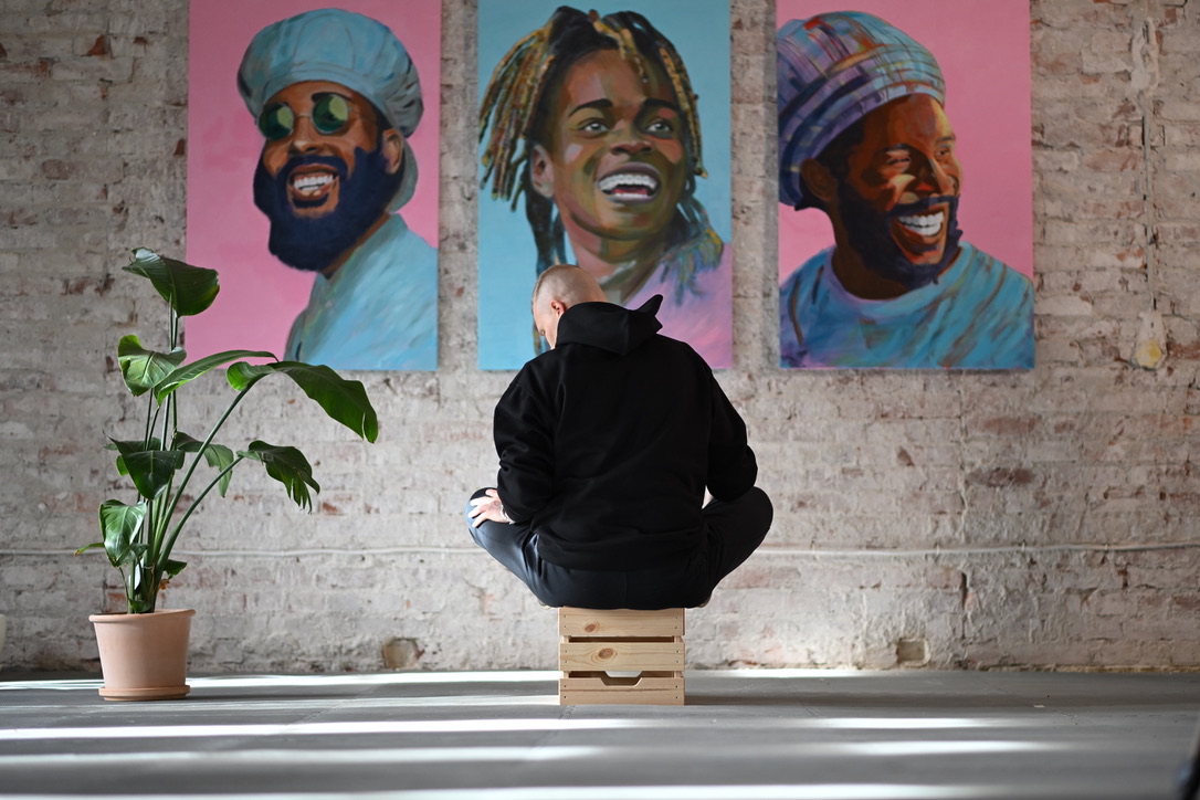 Artist seated facing three reggae portrait paintings